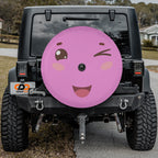 A black Jeep Wrangler with a large, colorful wheel cover featuring a smiling face and a winking eye.