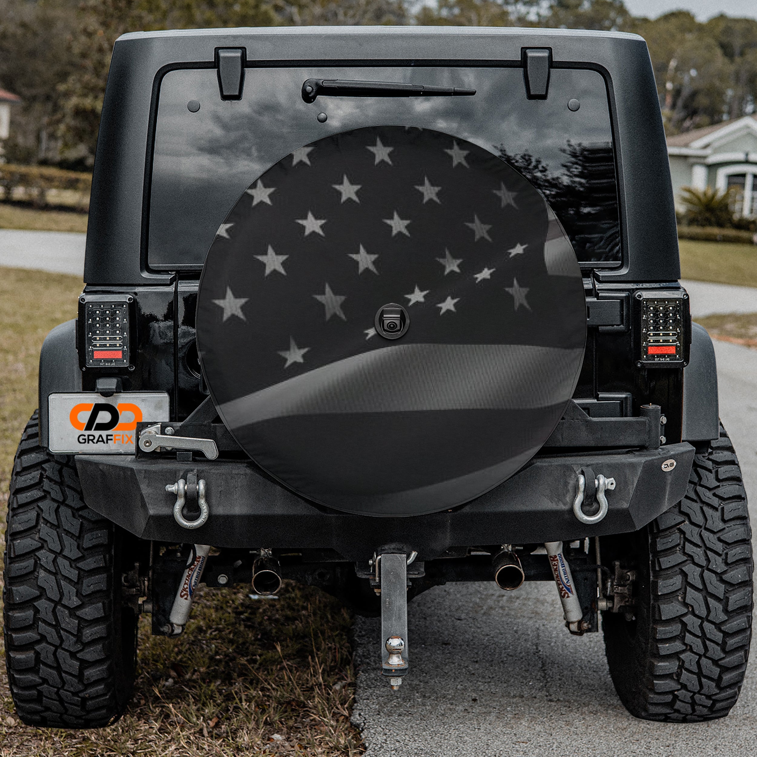 Wavey No Quarter American flag spare tire cover on black Jeep Wrangler with Graffix plate in driveway setting