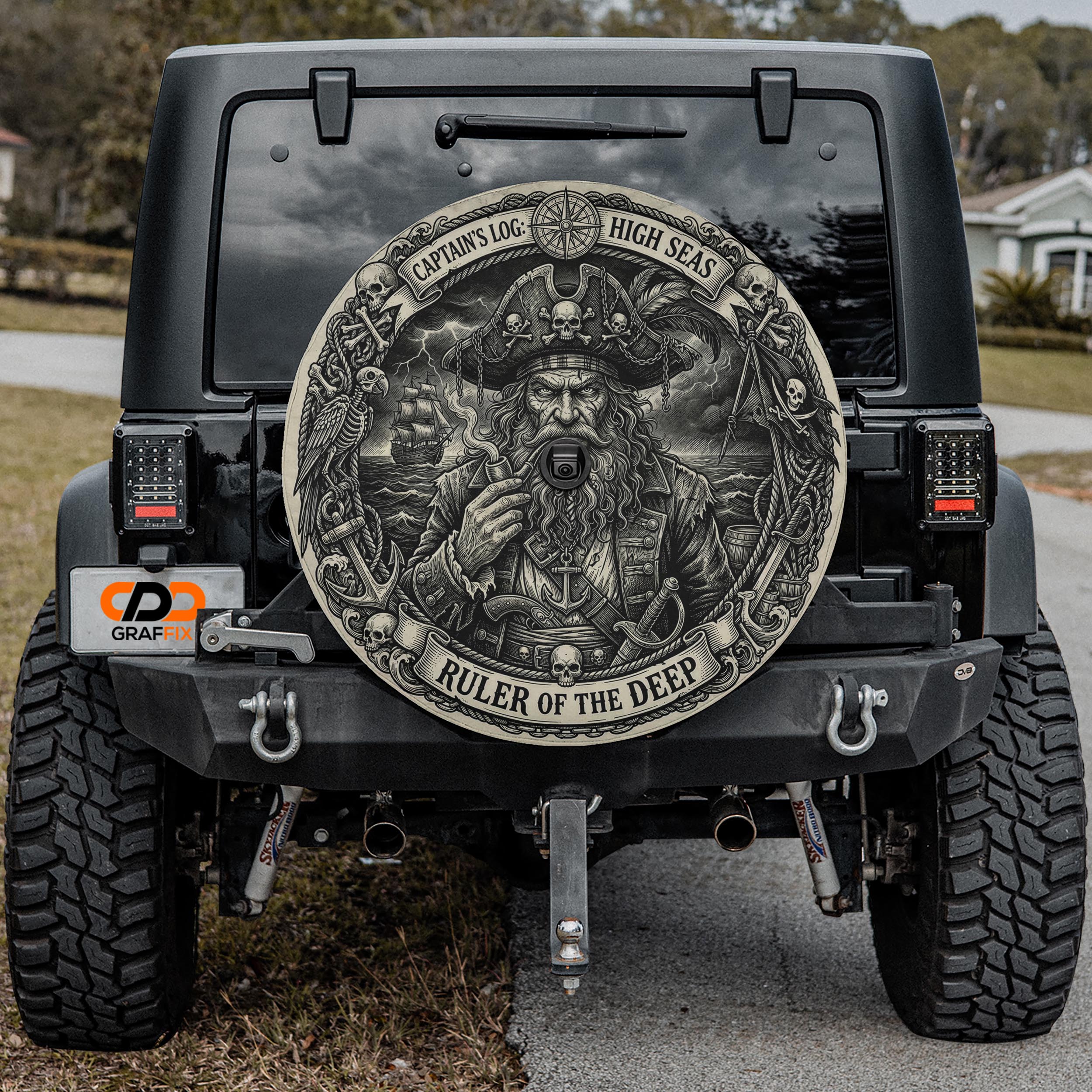 a black Jeep Wrangler with a large, detailed, pirate-themed wheel cover on the rear of the vehicle.
