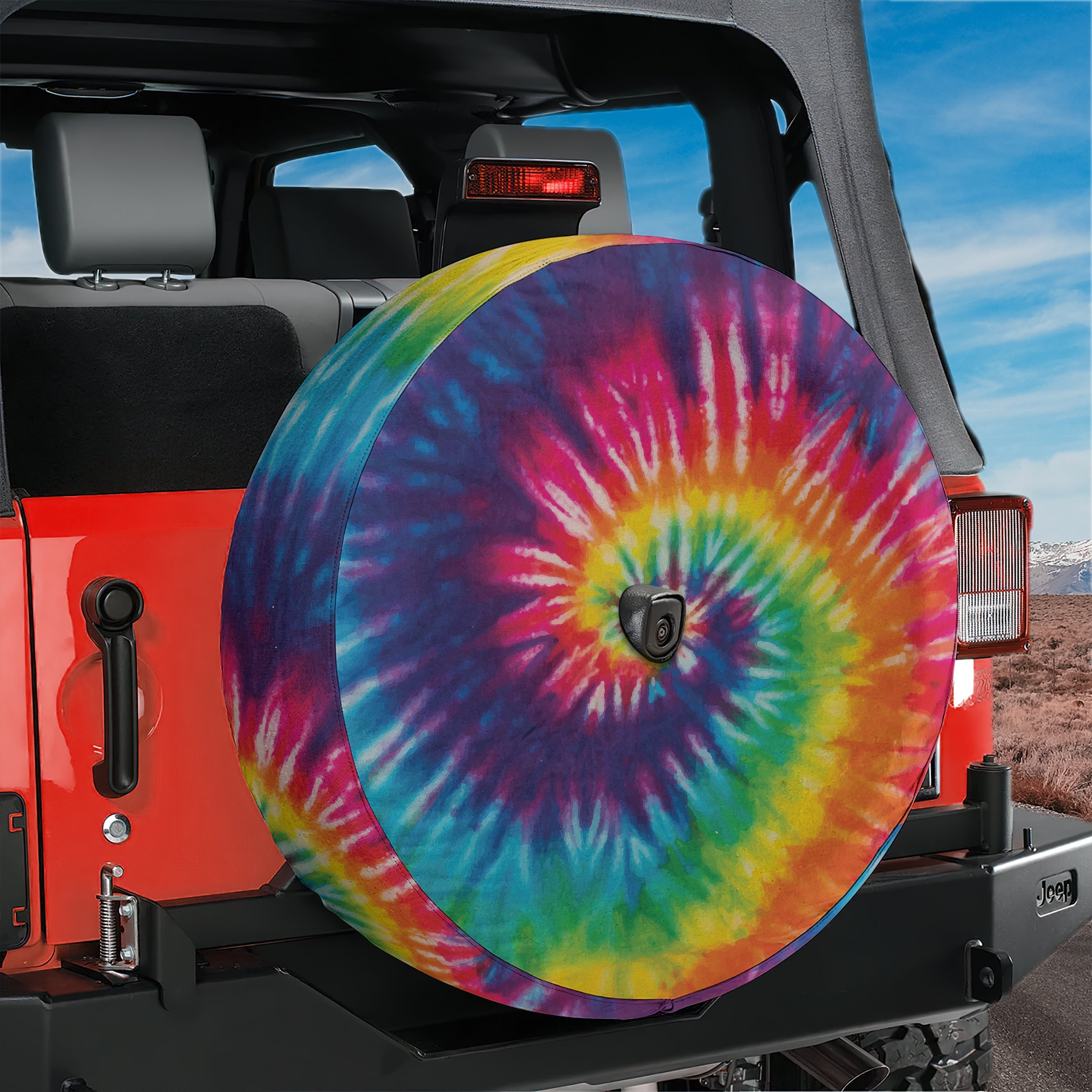 Rainbow spiral tie-dye spare tire cover mounted on red Jeep Wrangler rear with mountain horizon view