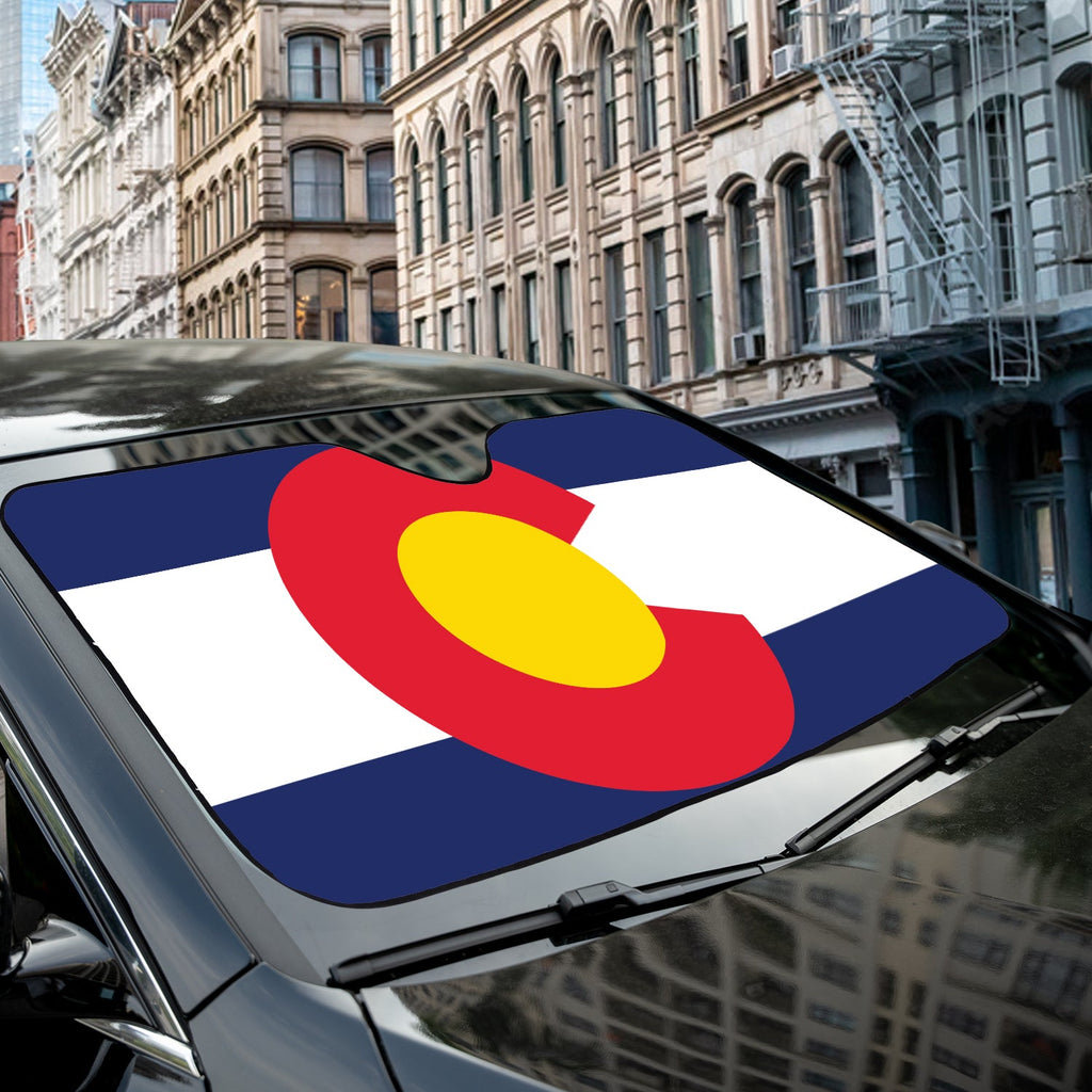 Colorado state flag accordion sunshade fitted across a sedan windshield on a sunlit urban brick street block