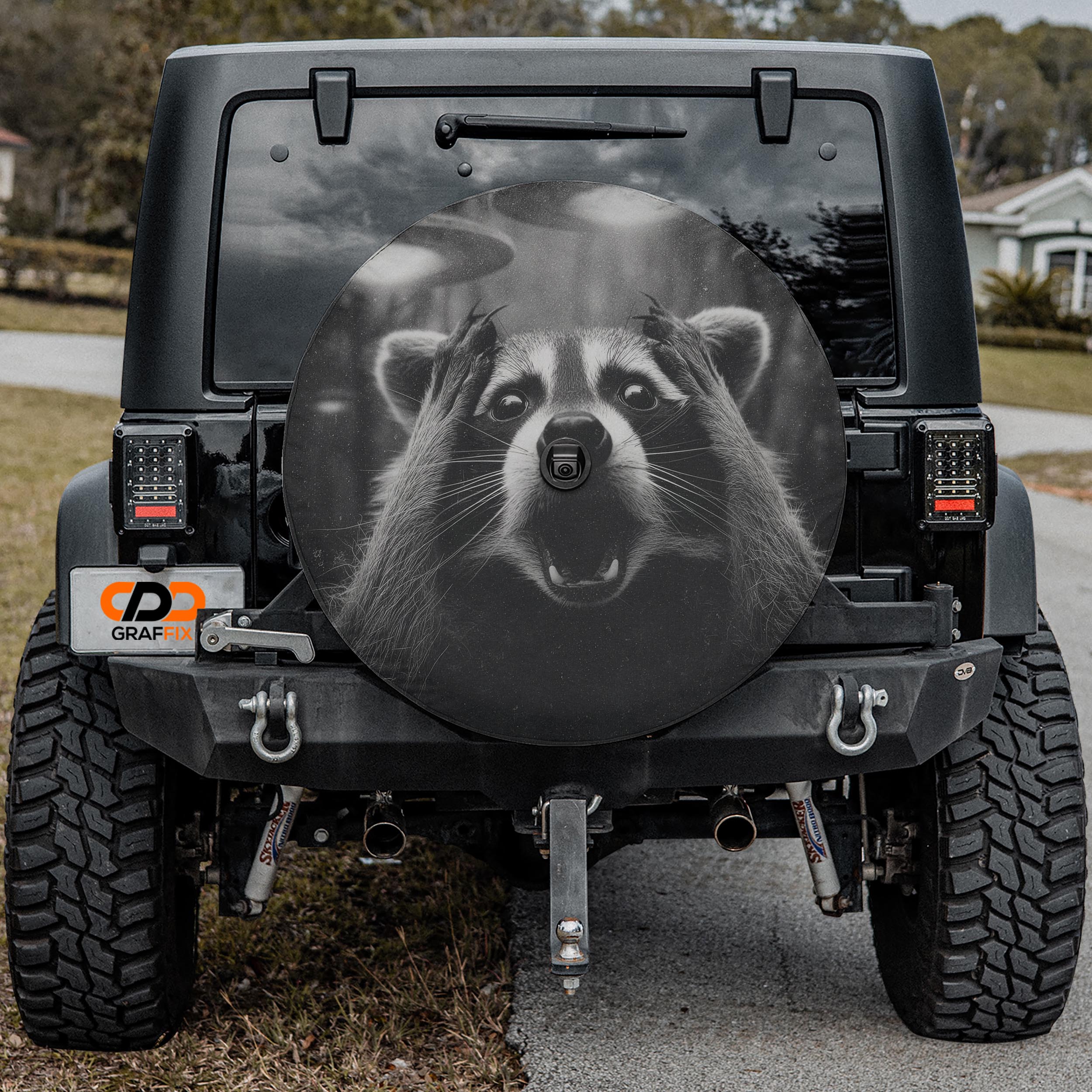 a black Jeep Wrangler with a large tire cover featuring a raccoon's face.