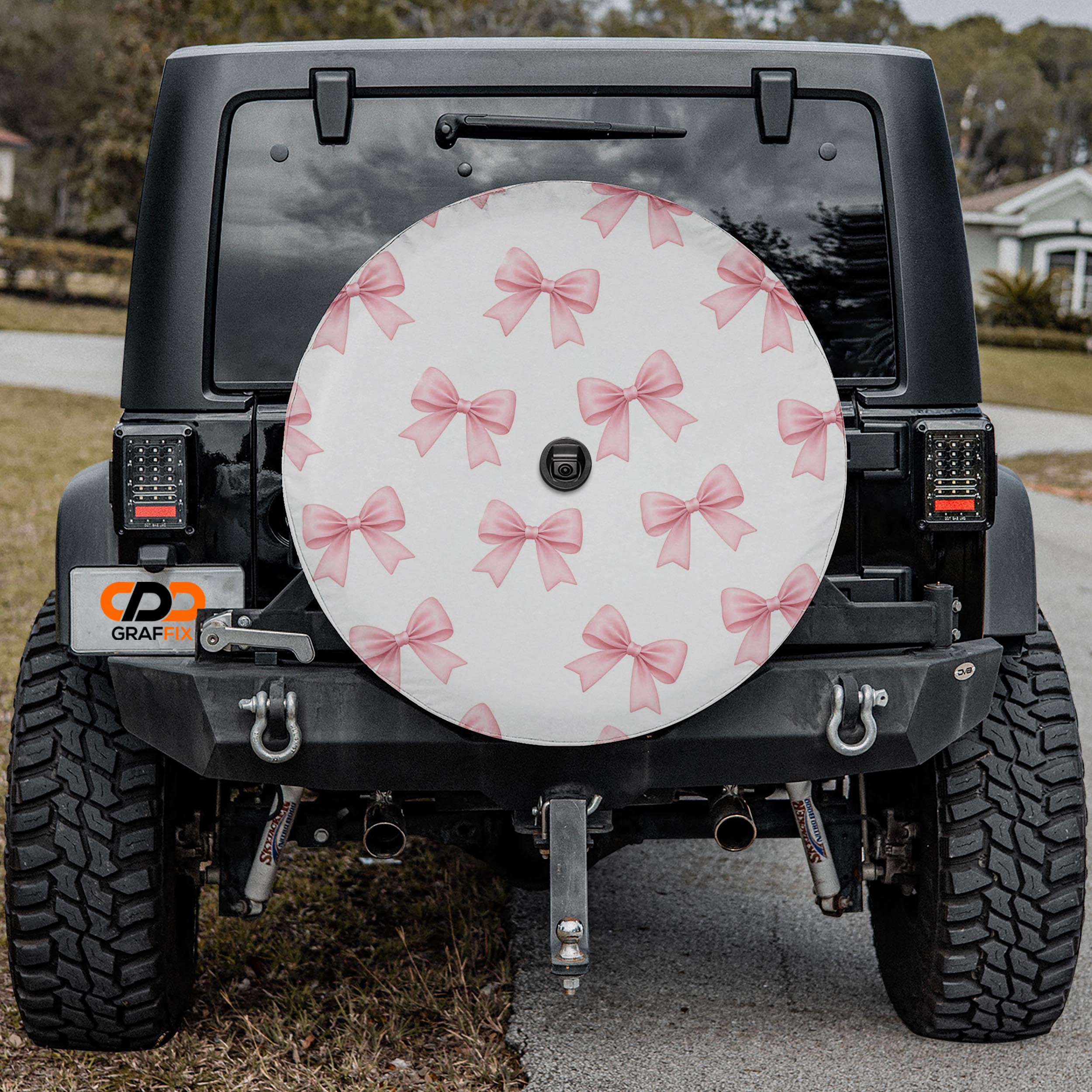 the back of a black Jeep Wrangler with a large white and pink bow-patterned wheel cover attached to the vehicle.