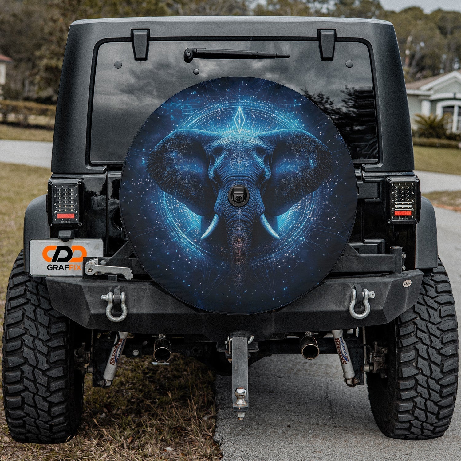 Spiritual Elephant blue mandala tire cover on black Jeep Wrangler rear in driveway with houses behind