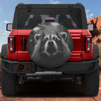 a red Jeep Wrangler with a large tire cover depicting a raccoon's face.