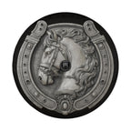 A decorative metal horseshoe with a detailed horse head design, featuring a chain and a small black object.