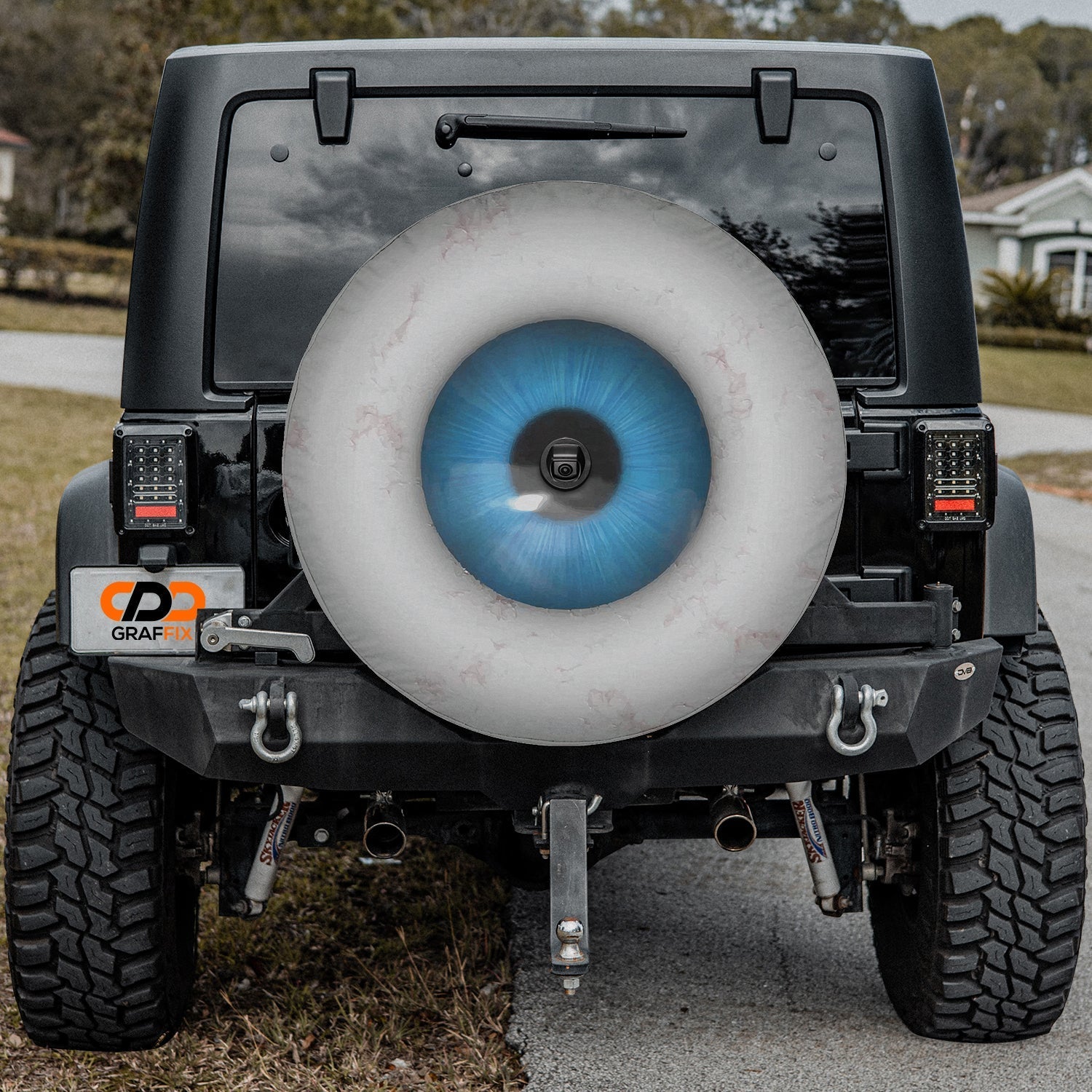 Eye On You spare tire cover mounted on a Jeep Wrangler rear wheel showing the iris design in driveway context