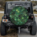 Green mermaid scale spare tire cover installed on a black Jeep Wrangler with GRAFFIX bumper logo display