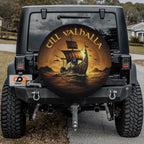 a black jeep with a large, round spare tire cover on the rear. The cover has a design of a ship sailing on the ocean, with the words "Till Valhall" written on it.