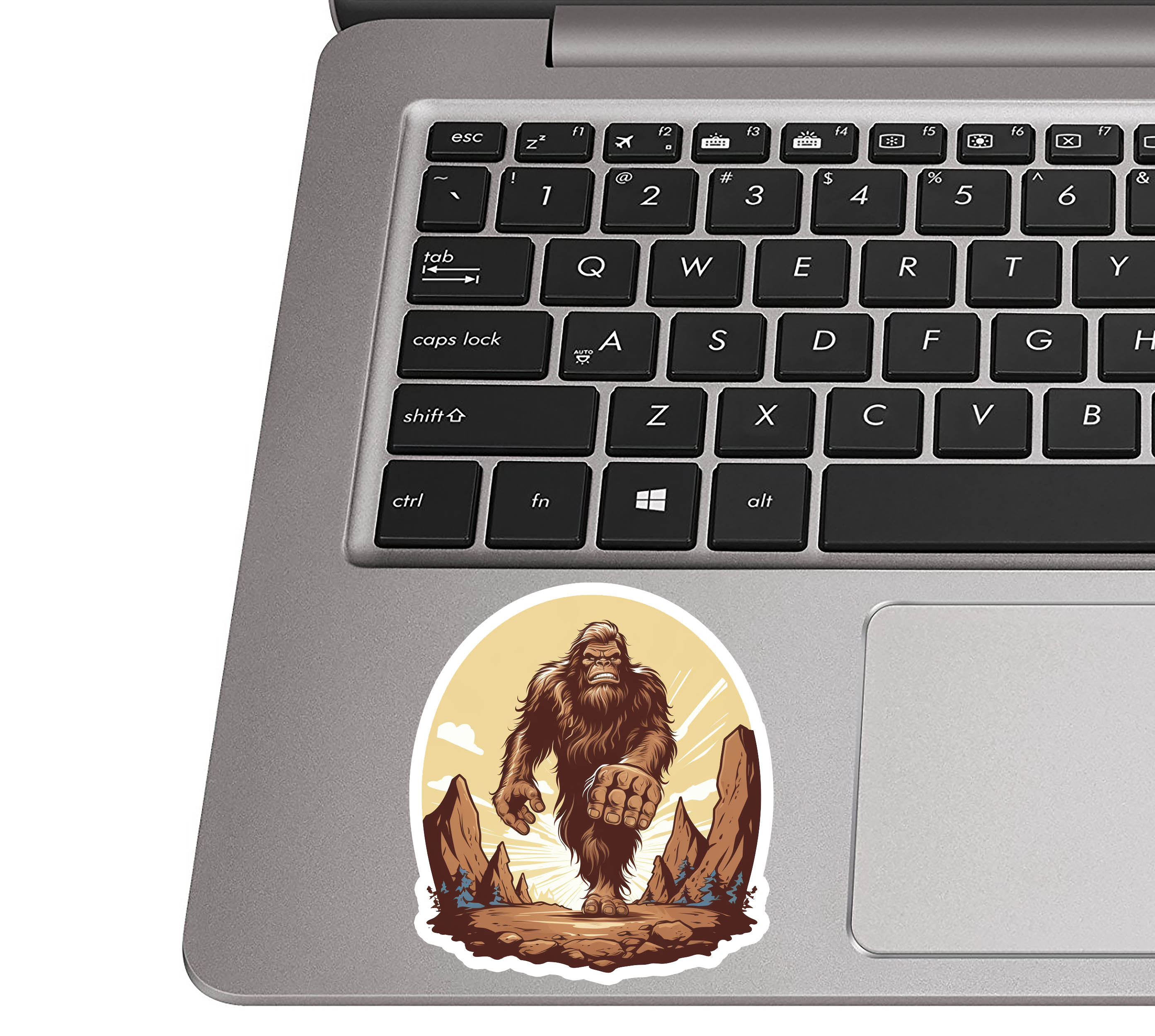 Bigfoot-horizon sticker stuck to a silver laptop palm rest beside a QWERTY keyboard to show sticker dimensions