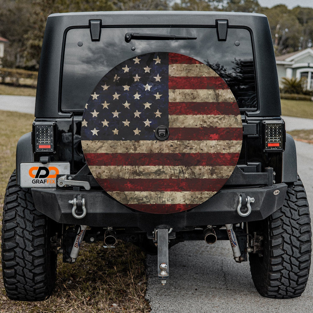 Rustic American flag spare tire cover on red Jeep Wrangler with desert backdrop featuring weathered patriotic design