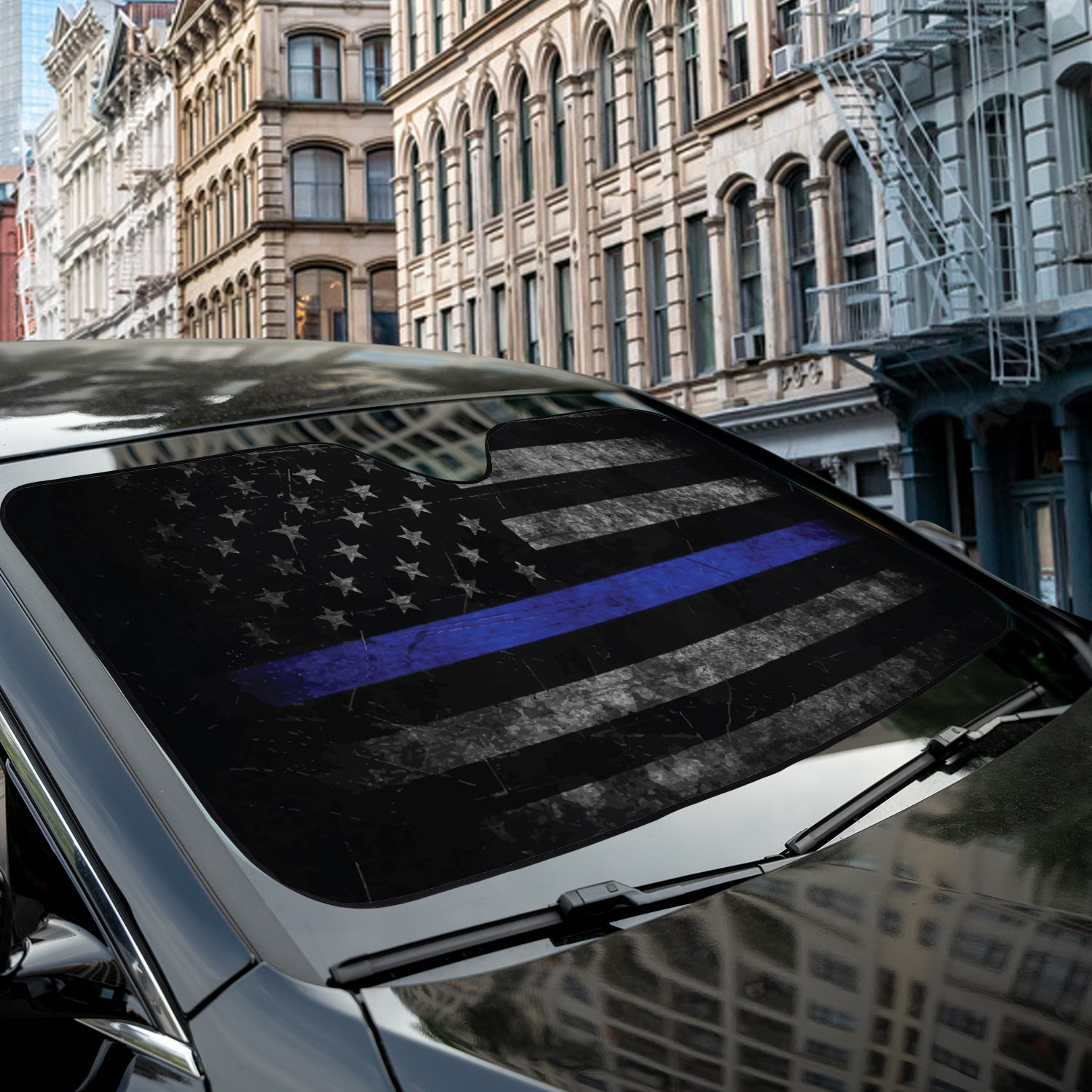 Thin Blue Line American Flag accordion sunshade close-up installed on a dark sedan windshield exterior view