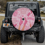 the back of a black Jeep Wrangler with a large, colorful wheel cover featuring various pink and white designs and text.