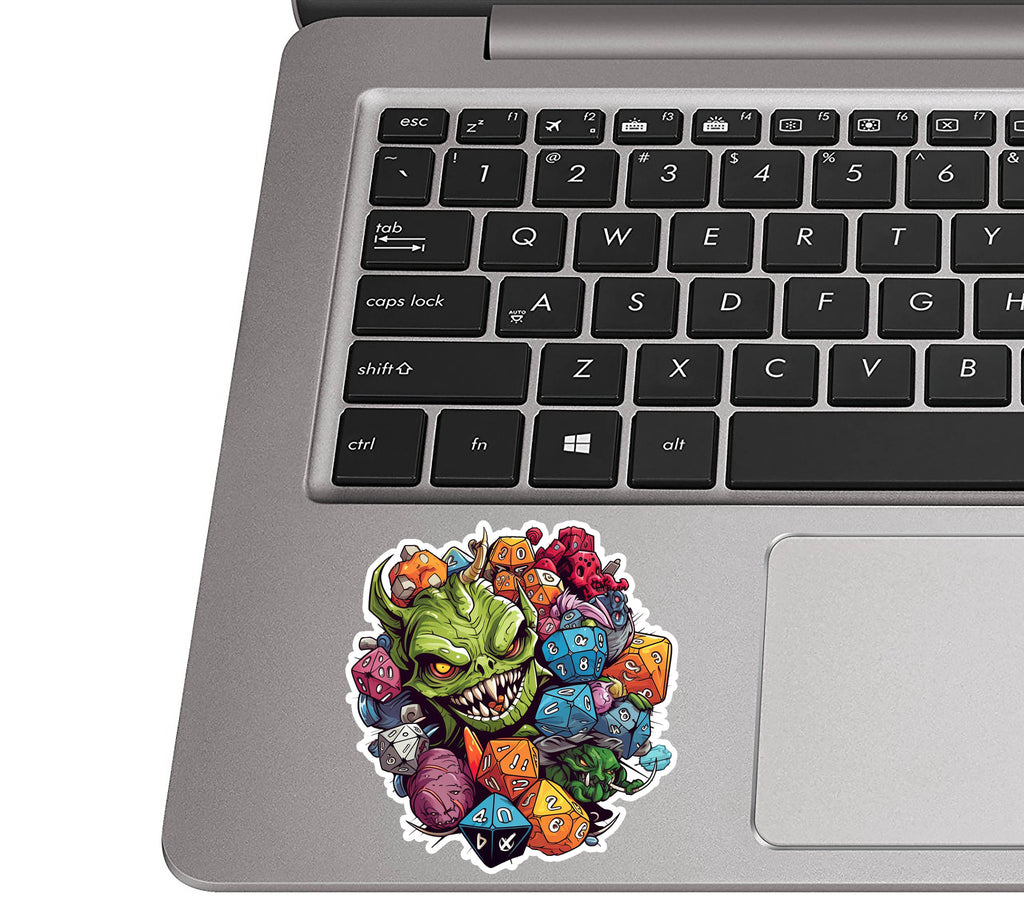 Goblin and D&D dice sticker applied to a silver laptop palm rest beside a QWERTY keyboard for scale view