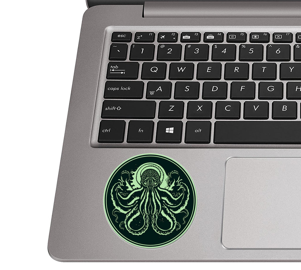 Minimalist Cthulhu green octopus circle sticker on silver laptop palm rest beside black QWERTY keys for scale