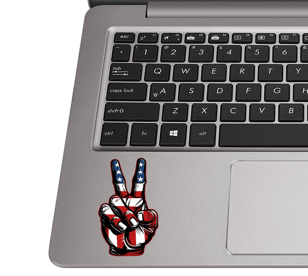 USA peace-sign hand sticker placed on a silver laptop palm rest beside a black QWERTY keyboard for scale view
