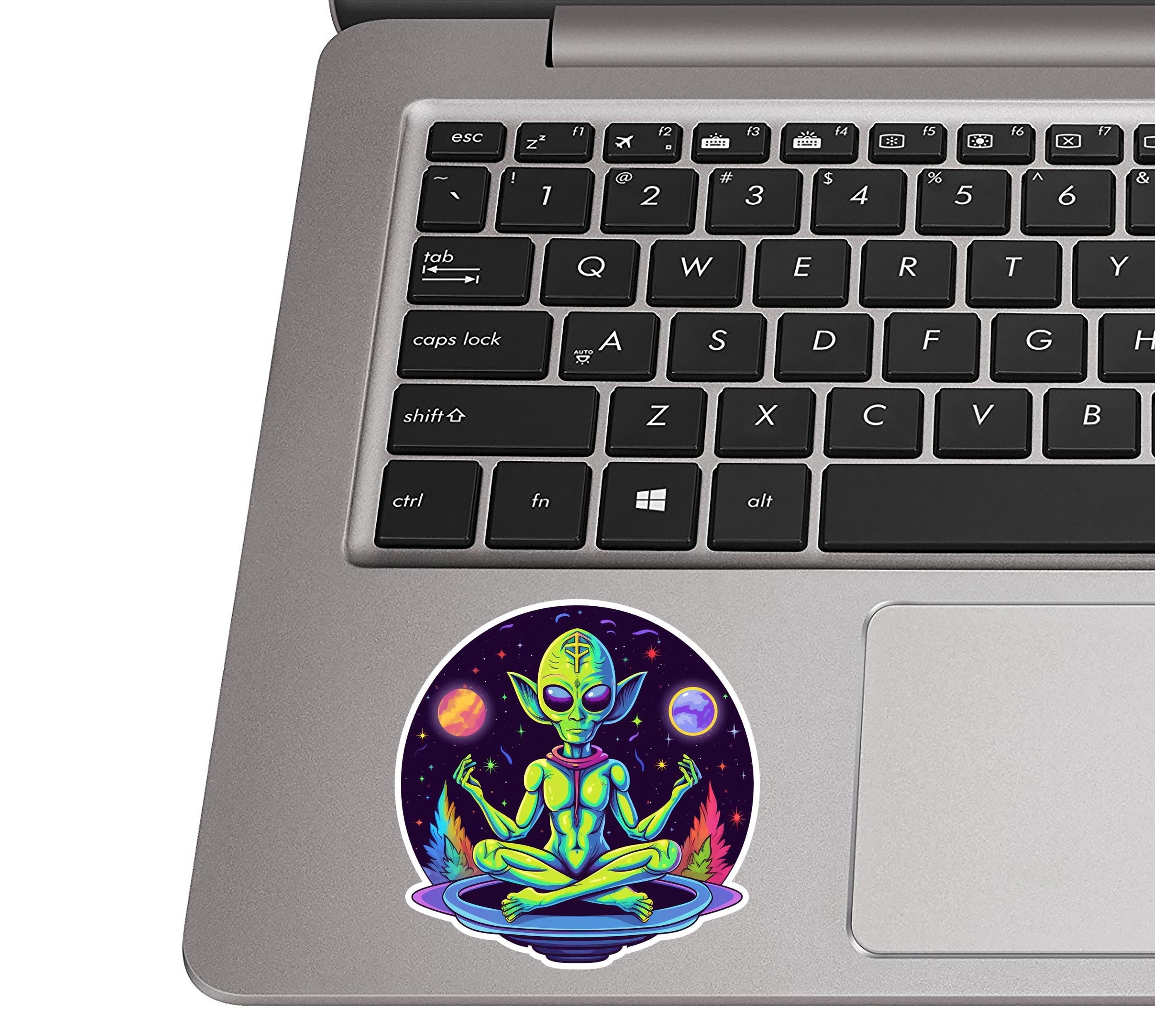 Psychedelic meditating alien sticker on a silver laptop palm rest near a black QWERTY keyboard for size scale