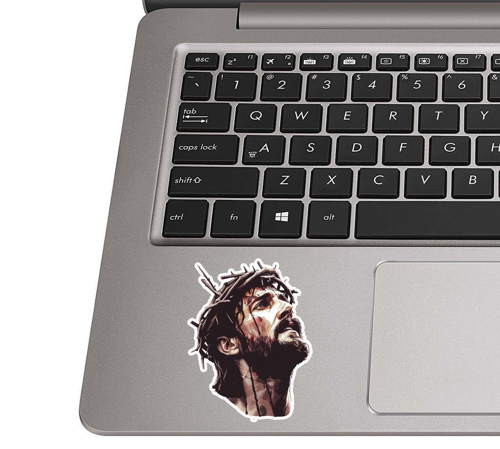 Jesus crown of thorns sticker placed on a silver laptop palm rest beside a black QWERTY keyboard for scale
