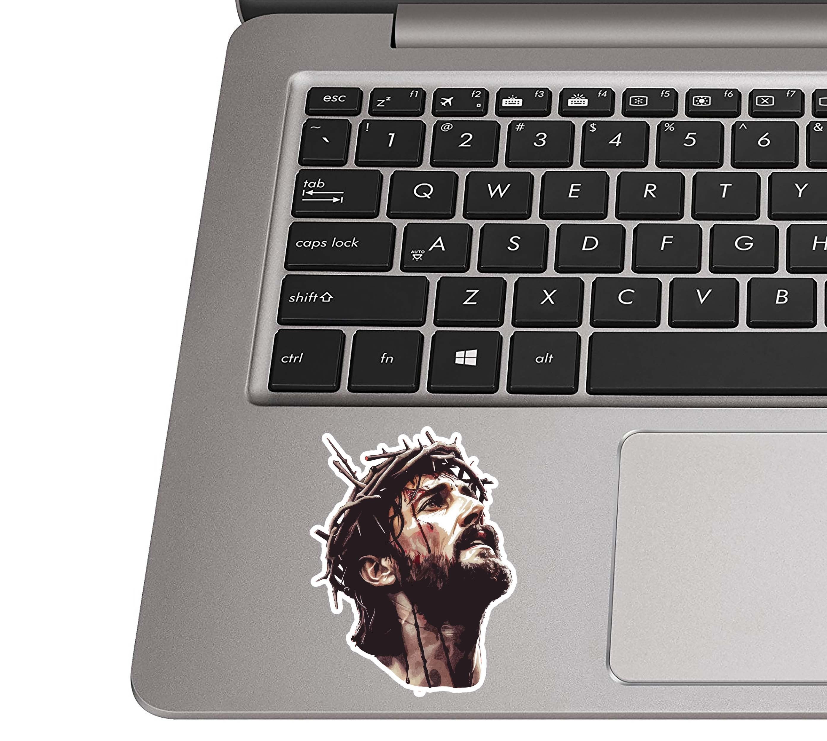 Jesus crown of thorns sticker placed on a silver laptop palm rest beside a black QWERTY keyboard for scale