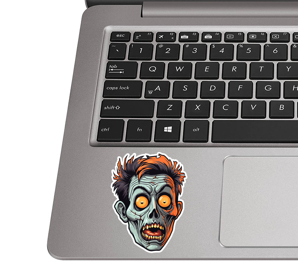 Zombie face sticker stuck on a silver laptop palm rest by the trackpad showing realistic applied sticker scale