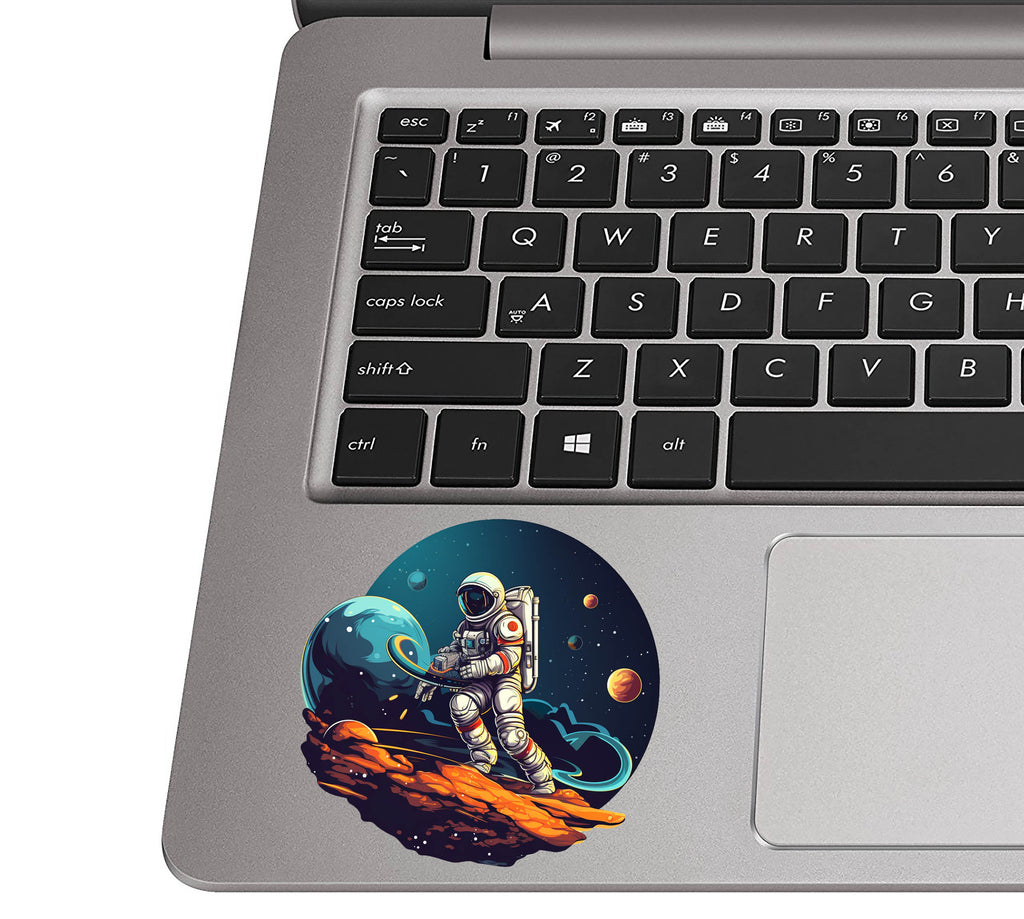 Asteroid-riding astronaut sticker on a silver laptop palm rest near a black QWERTY keyboard for scale